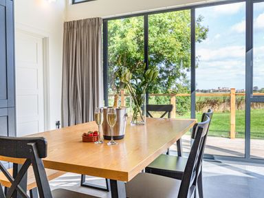 A dining table with champagne glasses strawberries and flowers by large windows showing a garden at Shearwater Lodge in Bamburgh