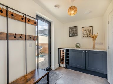 A hallway with a wooden bench and coat hooks next to a glass door and cabinets with decorative items at Shearwater Lodge in Bamburgh
