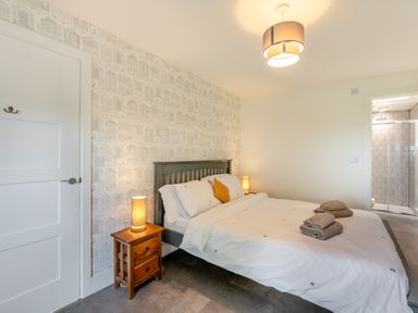 A bedroom with a double bed wooden bedside tables two lamps and an en suite bathroom at Shearwater Lodge in Bamburgh