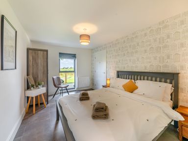 A bedroom with a double bed towels on the bed a chair a wardrobe and a door with a window showing outdoor greenery at Shearwater Lodge in Bamburgh