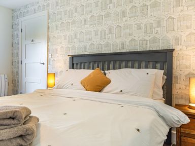 A bedroom with a black bed frame white bedding a mustard pillow lamps on wooden bedside tables and towels at Shearwater Lodge in Bamburgh
