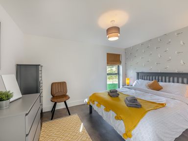 A bedroom with a bed with yellow throw and towels beside a window and a dresser with a mirror at Shearwater Lodge in Bamburgh