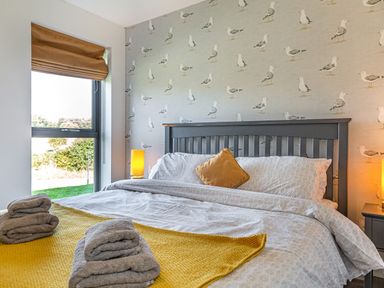 A bedroom with a grey wooden bedframe yellow pillow and towels with seagull wallpaper at Shearwater Lodge in Bamburgh