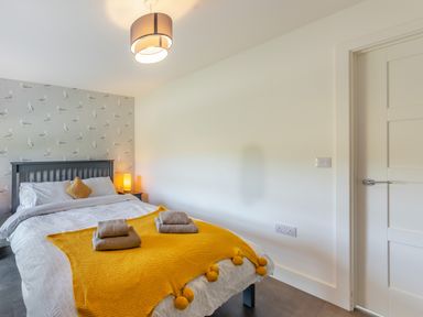 A bedroom with a bed covered with white and yellow bedding beside a side table with a lamp at Shearwater Lodge in Bamburgh