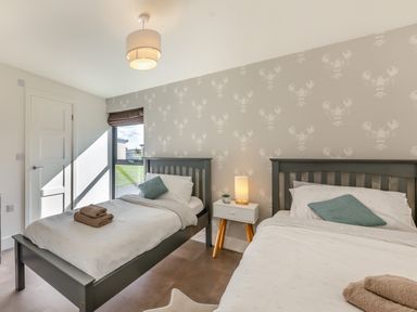 A bedroom with two single beds a nightstand with a lamp and a window at Shearwater Lodge in Bamburgh