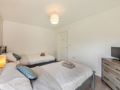 A bedroom with two beds a wooden dresser with a television and a ceiling light at Shearwater Lodge in Bamburgh