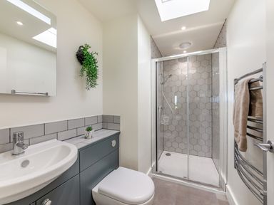 A bathroom with a sink, toilet, shower with hexagonal tiles, and a towel rail at Shearwater Lodge in Bamburgh