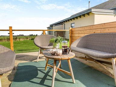 An outdoor patio with a wooden table set with coffee cups and a coffee press surrounded by wicker chairs at Shearwater Lodge in Bamburgh