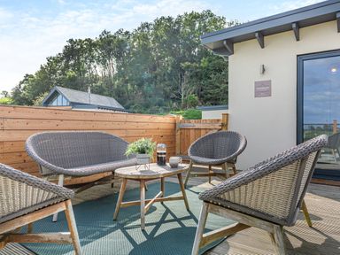 An outdoor seating area with wicker furniture including chairs and a loveseat around a wooden table on a deck at Shearwater Lodge in Bamburgh