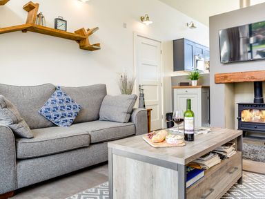 A living room with a gray sofa and a wooden coffee table with wine and food by a fireplace at Shearwater Lodge in Bamburgh
