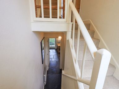 A stairway with beige carpet and white railing leading down to a hallway with stone tile flooring at Brook Cottage in Windermere