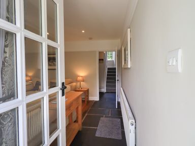 A hallway with a wooden table and lamp leading to a living room and staircase inside Brook Cottage in Windermere