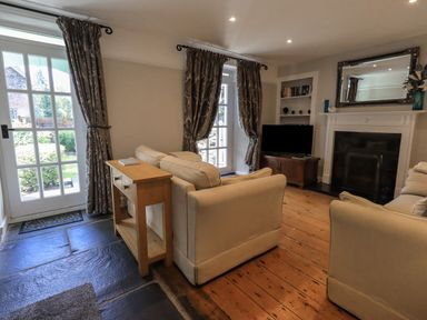 A living room with beige sofas a wooden console table a fireplace and a television at Brook Cottage in Windermere