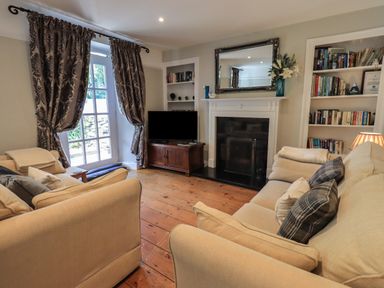 A living room with two beige sofas a fireplace a television bookshelves and patterned curtains at Brook Cottage in Windermere