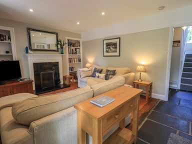 A living room with beige sofas a fireplace bookshelves and a wooden table at Brook Cottage in Windermere