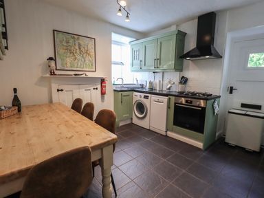 A kitchen with a wooden dining table and chairs green cabinets washing machine oven and tiled floor at Brook Cottage in Windermere