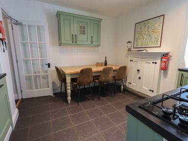 A kitchen with a wooden dining table and four brown chairs green cabinets a glass door and a map on the wall at Brook Cottage in Windermere
