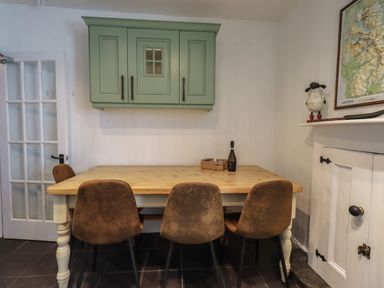 A kitchen with a wooden table and four brown chairs with green cupboards on the wall at Brook Cottage in Windermere