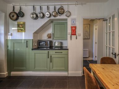 A kitchen with green cabinets pans hanging on a rail toaster and microwave on the counter at Brook Cottage in Windermere