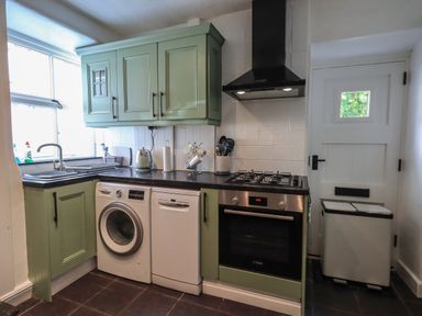 A kitchen with green cabinets, washing machine, dishwasher, oven, stove, and a white door at Brook Cottage in Windermere