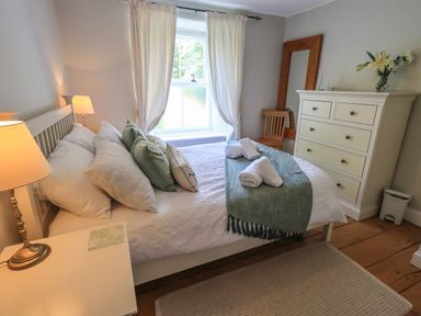 A bedroom with a bed with pillows and towels near a window and a dresser with a mirror and flowers at Brook Cottage in Windermere