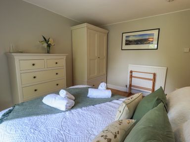 A bedroom with a bed with green and floral pillows a chest of drawers a wardrobe and a framed picture on the wall at Brook Cottage in Windermere