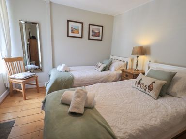 A bedroom with two single beds bedside lamp wooden chair and framed pictures at Brook Cottage in Windermere