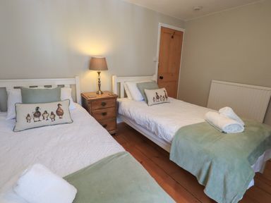 A bedroom with two single beds a wooden nightstand with a lamp and wooden door at Brook Cottage in Windermere