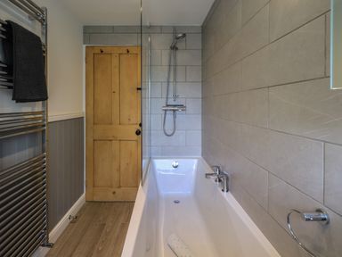 A bathroom with a bathtub shower wooden door tiled walls and a towel rack at Brook Cottage in Windermere