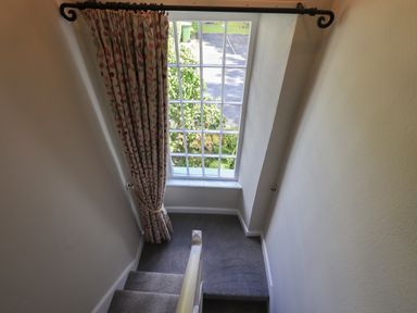 A carpeted staircase leading to a large window with patterned curtains at Brook Cottage in Windermere
