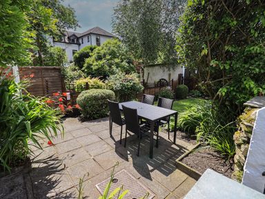 A garden patio with a black table and four chairs surrounded by plants and shrubs at Brook Cottage in Windermere