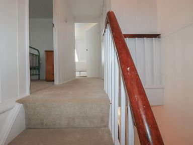 A staircase leading to a hallway with a bed and doorway at 84 Fore Street 