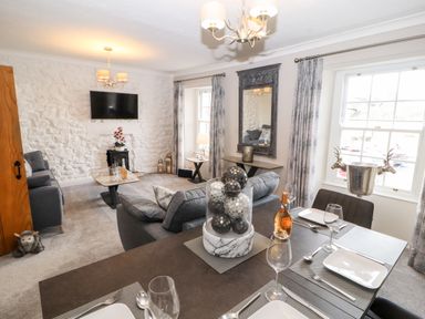 A dining table set with plates and wine glasses next to a living area with sofas and a wall-mounted TV at Market Square Maisonette in Kirkby Lonsdale