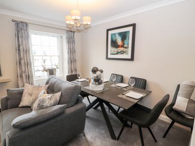 A dining room with a table set for four and a grey sofa at Market Square Maisonette in Kirkby Lonsdale