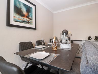 A dining table set with plates wine glasses and cutlery with a centerpiece and chairs in a dining room at Market Square Maisonette in Kirkby Lonsdale