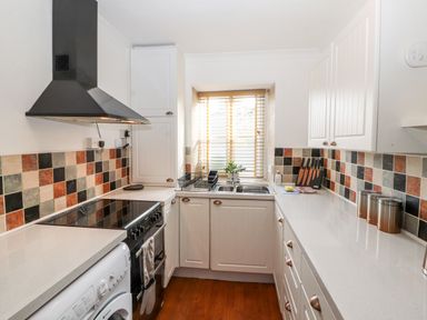 A kitchen with white cabinets stove washing machine and a window with blinds at Market Square Maisonette in Kirkby Lonsdale