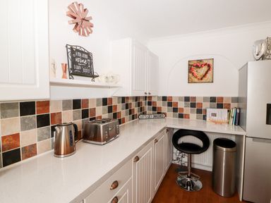A kitchen corner with countertop appliances, a bar stool, a trash bin, cabinets, and a tiled backsplash at Market Square Maisonette in Kirkby Lonsdale