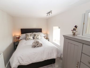 A bedroom with a bed with pillows and rolled towels bedside tables with lamps a window and a dresser at Market Square Maisonette in Kirkby Lonsdale