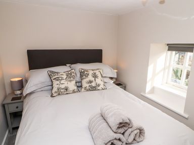 A bedroom with a bed with patterned cushions and folded towels by a window at Market Square Maisonette in Kirkby Lonsdale