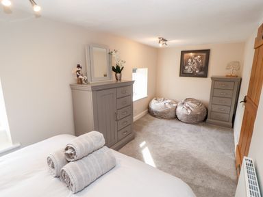 A bedroom with a bed with rolled towels a tall dresser with a mirror two bean bags a chest of drawers and framed artwork at Market Square Maisonette in Kirkby Lonsdale