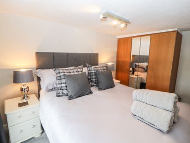 A bedroom with a bed with pillows and folded towels bedside tables with lamps and a wardrobe with mirrors at Market Square Maisonette in Kirkby Lonsdale