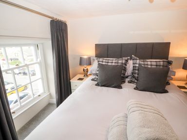A bedroom with a bed pillows bedside tables lamps and a window with curtains at Market Square Maisonette in Kirkby Lonsdale