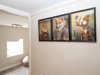 A hallway with three framed pictures of animals in clothing and a window in an adjacent room at Market Square Maisonette in Kirkby Lonsdale