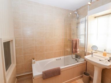 A bathroom with a bathtub shower combination a sink with a mirror and soap dispenser at Market Square Maisonette in Kirkby Lonsdale