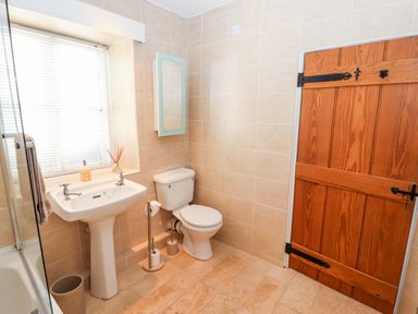 A bathroom with a white pedestal sink and toilet a wooden door and window blinds at Market Square Maisonette in Kirkby Lonsdale