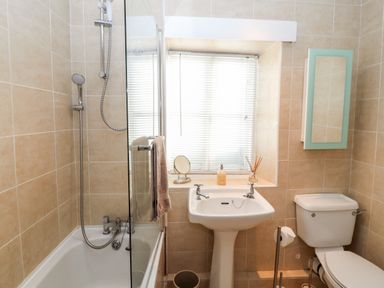 A bathroom with a bathtub shower combination a pedestal sink a toilet and a window at Market Square Maisonette in Kirkby Lonsdale