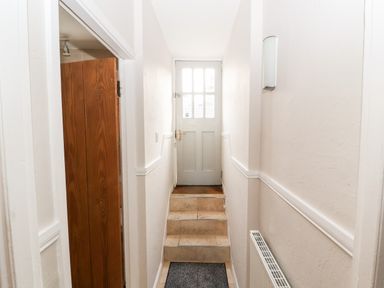 A hallway with stairs leading to a door with glass panels and a wooden door on the left at Market Square Maisonette in Kirkby Lonsdale