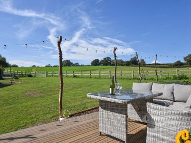 A garden with a wooden deck a gray wicker table and sofa with a wine bottle and glasses at Maple in Wootton Fitzpaine near Charmouth