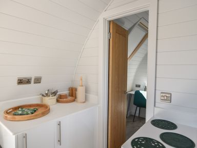 A kitchen counter with cutlery holder and paper towel near a wooden door leading to a room with a chair at Maple in Wootton Fitzpaine near Charmouth