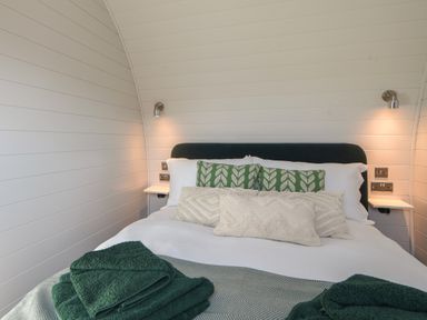 A bedroom with a bed with white and patterned pillows dark headboard wall lamps and green towels on the bed at Maple in Wootton Fitzpaine near Charmouth